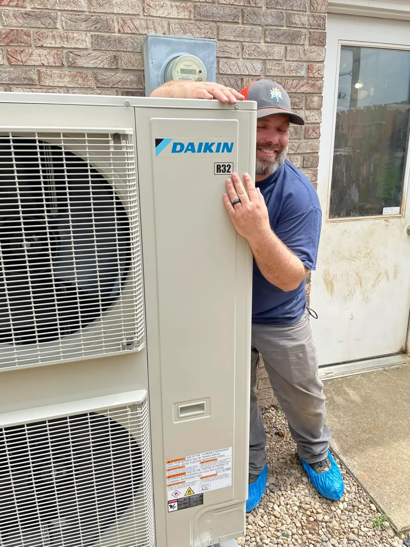 Polley's Perfect Seasons certified Daikin Fit installer standing beside a brand-new R32 Daikin outdoor unit at a Plainfield, IN home