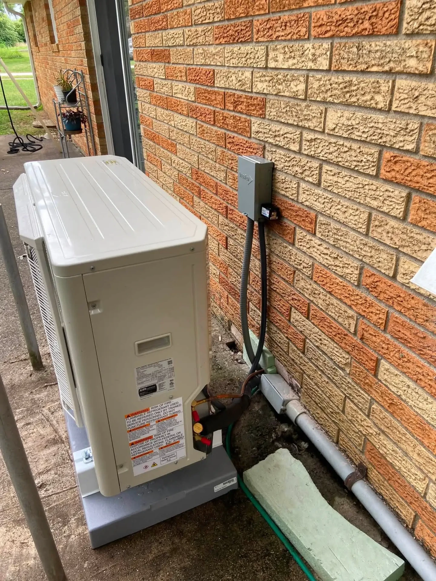 Ductless mini split outdoor unit with electrical disconnect and line set conduit on a brick home in Avon, Indiana