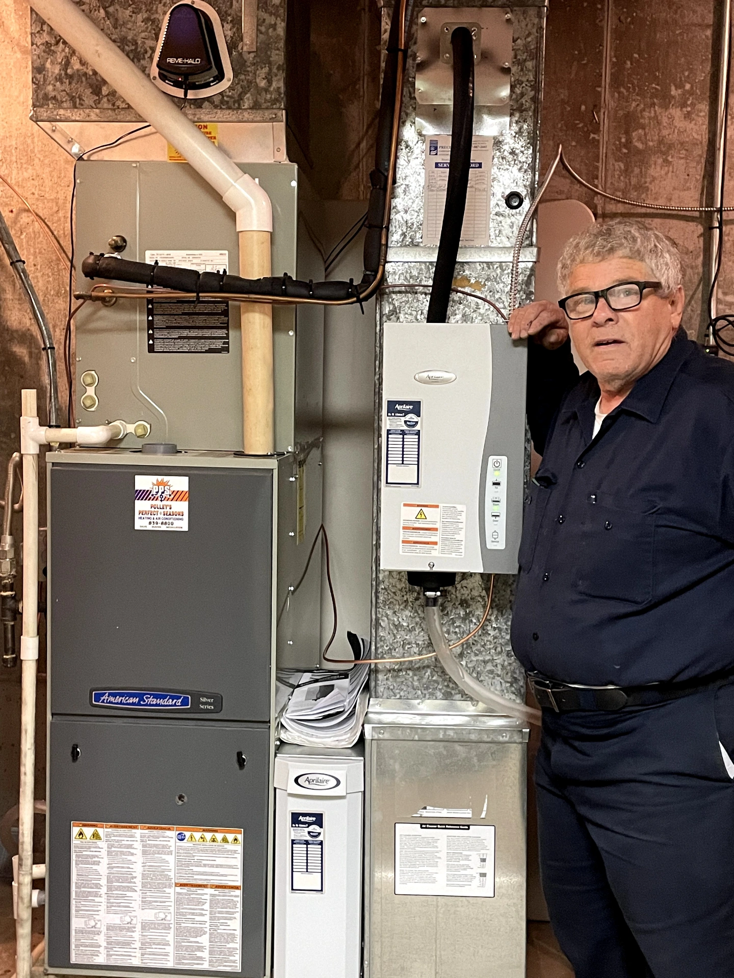 Polley's Perfect Seasons technician standing next to a newly installed American Standard furnace and AprilAire whole-home humidifier in a Plainfield, IN basement